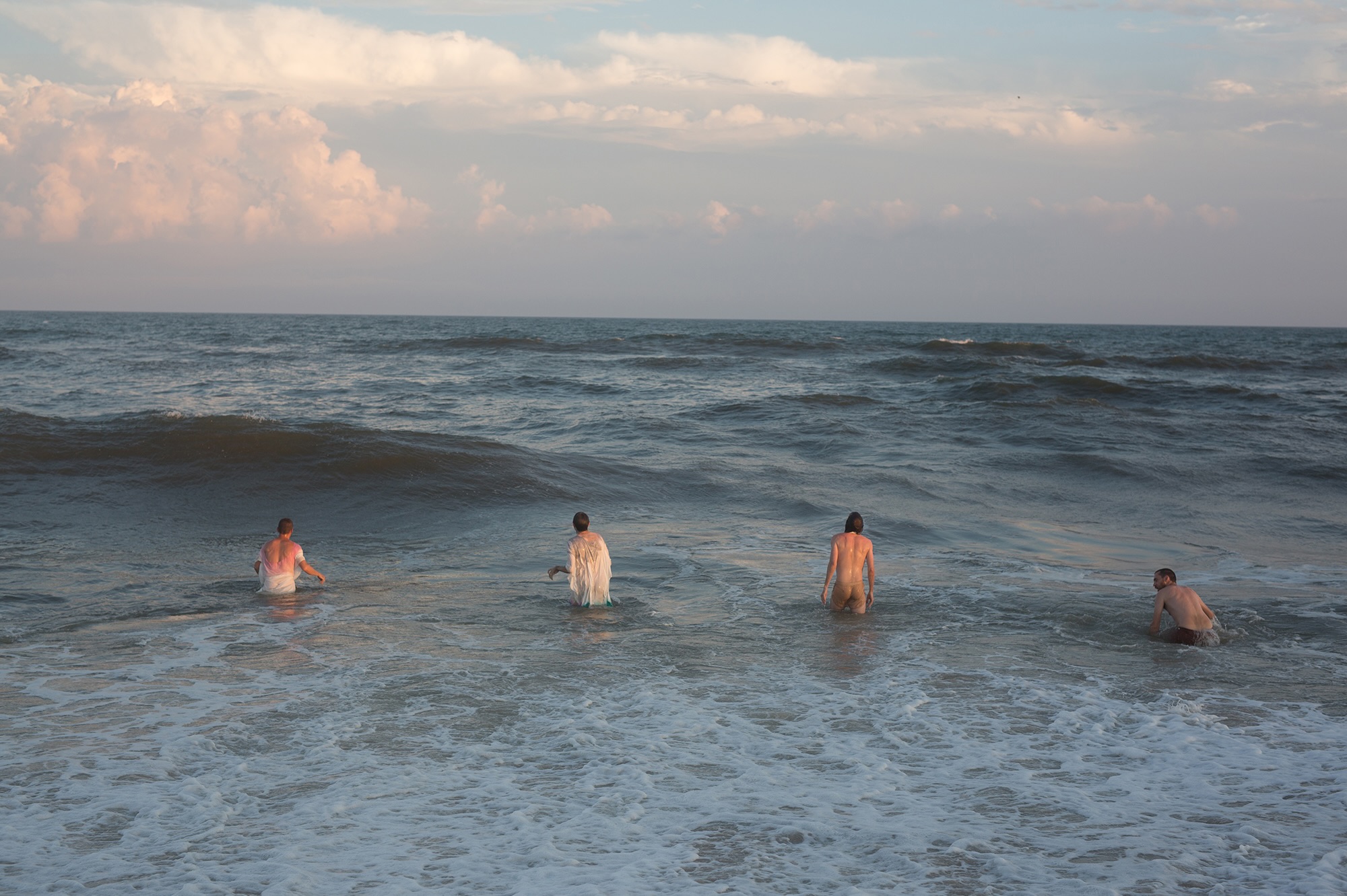 Four people stand in the ocean beneath a pale evening sky.
